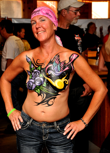 woman with a very detailed and colorful body painting featuring blue roses a colorful bird